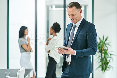 Buy stock photo Cropped shot of a mature businessman looking at a tablet in the office with his colleagues in the background