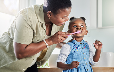 Buy stock photo Shot of a mother brushing her little daughter's teeth in the bathroom at home