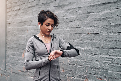 Buy stock photo Shot of a young woman checking her fitness tracker while out on a run outside