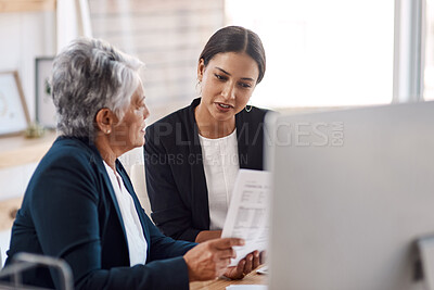 Buy stock photo Cropped shot of two attractive businesswomen looking over paperwork in their office