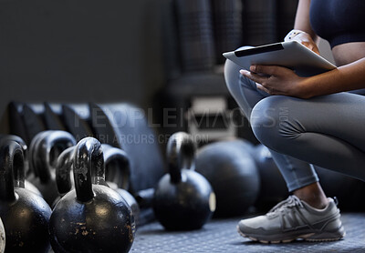 Buy stock photo Closeup shot of an unrecognisable woman using a digital tablet alongside kettlebells in a gym