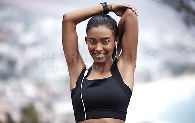 Buy stock photo Portrait of a sporty young woman wearing earphones and stretching her arms while exercising outdoors