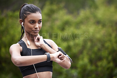 Buy stock photo Shot of a sporty young woman checking her pulse while exercising outdoors