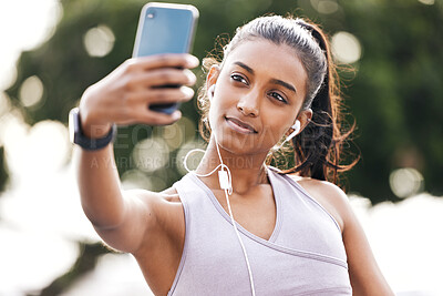 Buy stock photo Shot of a sporty young woman wearing earphones and taking selfies while exercising outdoors