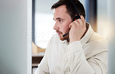 Buy stock photo Shot of a handsome young call centre agent sitting alone in his office and looking contemplative while using his computer