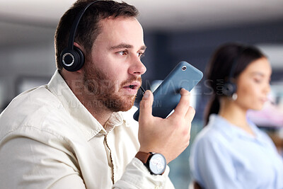 Buy stock photo Shot of a young call centre agent sitting in the office with his colleague and using his cellphone