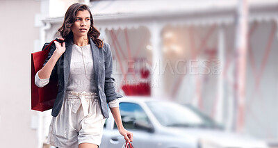 Buy stock photo Shot of a young woman walking through the city with shopping bags