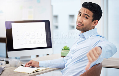 Buy stock photo Shot of a young businessman giving the thumbs down while working at his desk