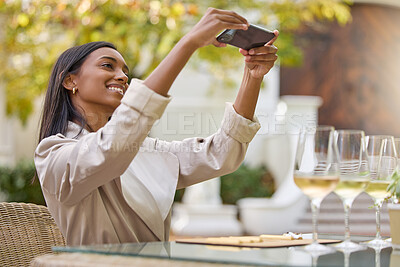 Buy stock photo Shot of an attractive young woman sitting alone during a wine tasting and using her cellphone to take a picture