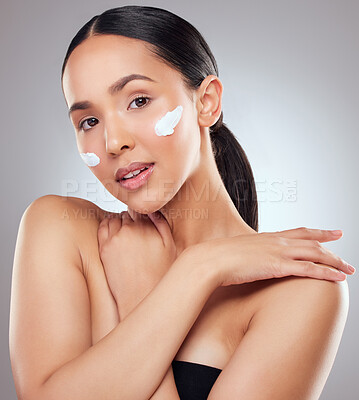 Buy stock photo Studio portrait of a beautiful young woman applying moisturiser to her face against a grey background