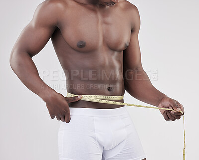 Buy stock photo Shot of a unrecognizable man measuring his waist using a measuring tape against a studio background