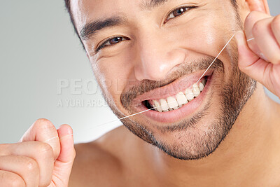 Buy stock photo Studio shot of a handsome young man flossing his teeth against a grey background