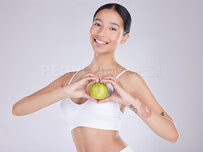 Buy stock photo Shot of an attractive young woman standing and holding an apple in the studio
