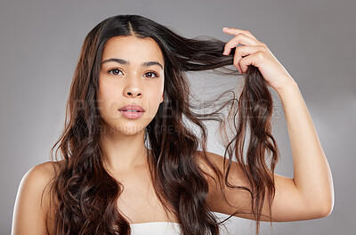 Buy stock photo Studio portrait of an attractive young woman holding her hair against a grey background