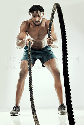 Buy stock photo Studio shot of an athletic young man working out with battle ropes