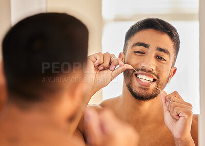 Buy stock photo Shot of a handsome young man standing alone and flossing in his bathroom at home