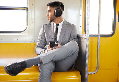 Buy stock photo Shot of a young businessman wearing headphones and using a cellphone while staring out the window on a train during his commute