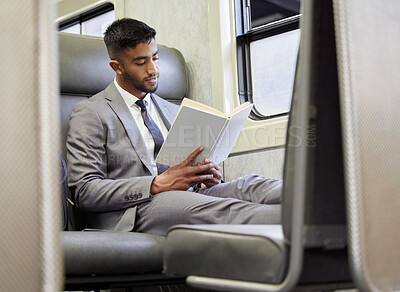 Buy stock photo Shot of a young businessman reading a book in a train during his commute
