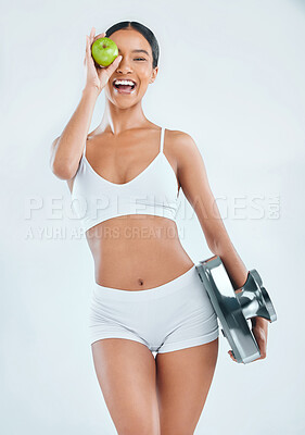 Buy stock photo Shot of an attractive young woman standing alone in the studio and posing with an apple and a scale