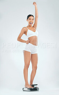 Buy stock photo Full length shot of an attractive young woman feeling excited while checking her weight on a scale in the studio