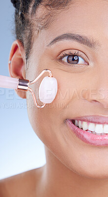 Buy stock photo Cropped portrait of an attractive young woman using a jade roller on her face against a blue background