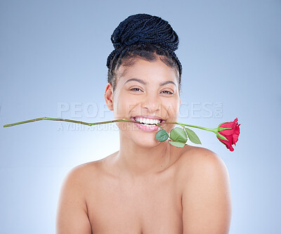 Buy stock photo Studio portrait of an attractive young woman holding a rose between her teeth against a blue background