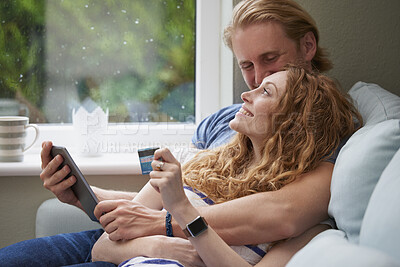 Buy stock photo A young happy couple snuggling while using a digital tablet to make online card payments