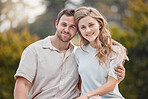 Portrait of young happy caucasian couple sitting together during a day outdoors. Handsome smiling man holding and embracing his beautiful wife in the garden. Showing love and affection while bonding