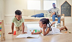 Little kids lying on the floor with toys and colouring in a book. Small african american brother and sister playing together at home while parents sit in the background