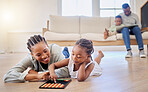 African american family bonding in the lounge together at home. Black mother playing a game with her daughter while a little boy is reading a book with his father in the background. Family having fun