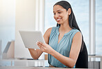 Young mixed race businesswoman smiling while working on a digital tablet in an office at work. One beautiful cheerful hispanic female boss using social media sitting at a desk