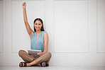 Cheerful young successful businesswoman using her wireless tablet device, sitting on the floor of her office raising her hand in celebration. Portrait of smiling hispanic business professional using a device to shop online while sitting with her legs cros