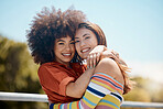 Portrait of two young mixed race female friends embracing each other and smiling outside on a sunny day. A Beautiful gay hispanic woman with a cool afro hair style showing affection by hugging her girlfriend while on a date