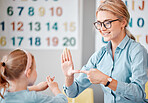 Smiling caucasian teacher wearing spectacles communicating with deaf girl student with hand sign language in a classroom at school. Sign language teacher in a tutoring class for a cute female child with hearing disability