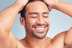 Smiling muscular asian man showering alone in a studio and washing his hair against a blue background. Fit and strong mixed race man standing under pouring water. Hispanic athlete enjoying hot shower