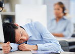 One exhausted asian male call centre agent sleeping at his desk in an office. Businessman feeling overworked, tired and demotivated while operating helpdesk. Lazy consultant slacking and ignoring clients by taking a nap. Burnout and stress in workplace