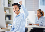 One happy young asian male call centre telemarketing agent cheering with joy and punching the air with fists while working in an office. Excited businessman celebrating successful sales and reaching targets to win