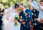 Newlywed couple bride and groom sharing a kiss while surrounded by friends and family and being showered with confetti rose petals after their wedding ceremony