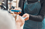 Closeup of a clerk accepting a credit card payment from a customer in a cafe or store. Hands of woman using card machine reader while taking money for a purchase transaction from a man in a shop