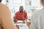 Group of diverse businesspeople having a meeting in a modern office at work. Young happy african american businessman wearing glasses talking about an idea while sitting in a boardroom with colleagues. Creative businesspeople planning together