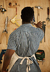 Back of carpenter picking a tool from his wall. African American entrepreneur deciding on a tool. Creative businessman picking a tool from his wall. Carpenter reaching for a tool from his collection