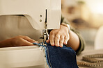 Closeup of the hand of a seamstress using a sewing machine. Fashion designer sewing denim fabric on a machine. Tailor using a sewing machine. Creative entrepreneur stitching a piece of material