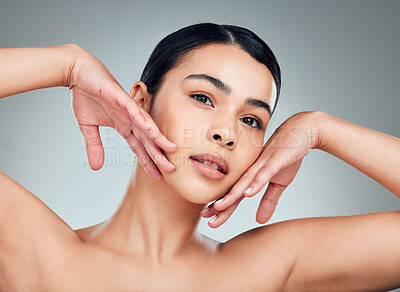 Buy stock photo Portrait of a beautiful mixed race woman touching smooth soft skin in a studio. Hispanic model with healthy natural glowing skin looking confident against grey copyspace while doing routine skincare