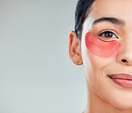 Studio closeup portrait of a beautiful mixed race woman wearing under eye patches. Hispanic model with glowing skin using hydrating treatment against a grey copyspace background