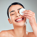 A beautiful happy mixed race woman using a cotton pad to remove makeup during a grooming routine. Hispanic woman applying toner to her face against grey copyspace background in a studio