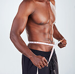 One unrecognizable African American fitness model posing topless with tape measure around his waist while looking muscular. Confident male athlete isolated on grey copyspace after positive weight loss