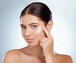 Portrait beautiful woman applying face cream while posing with copyspace. Caucasian model isolated against grey studio background with product on cheek. Moisturise and sunscreen for healthy skincare