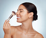 Beautiful woman holding and using cosmetic makeup brush to apply blush makeup while posing with copyspace. Caucasian model isolated against grey studio background. Getting ready after skincare routine