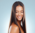 A hispanic brunette woman with long lush beautiful hair posing and smiling against a grey studio background. Mixed race female standing showing her beautiful healthy hair