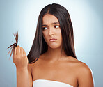 A young mixed race woman looking unhappy with her unhealthy hair against a grey background. Hispanic female expressing dissatisfaction at her split ends